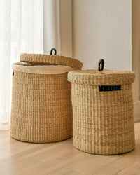 Two woven laundry baskets with lids on a wooden floor.