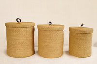 Three woven storage baskets with lids on a light background