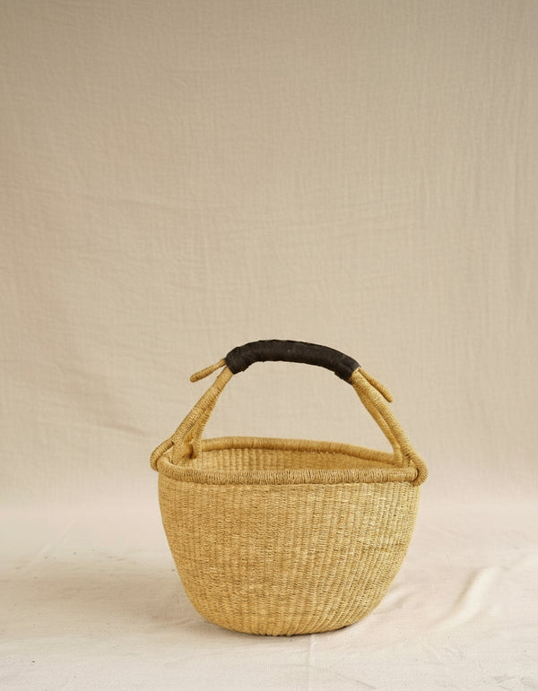 Woven basket with a black handle on a beige background