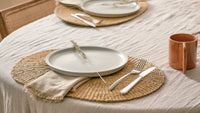 Dining table setting with plates, cutlery, and a mug on woven placemats.