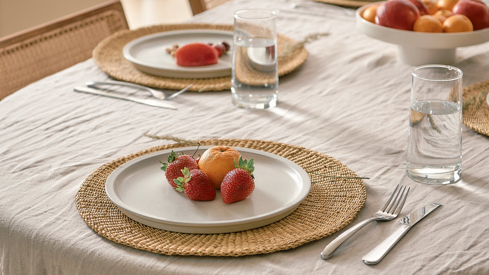 Dining table setting with plates, glasses, and fruit on a textured tablecloth.
