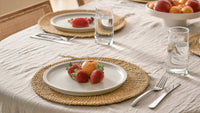 Dining table setting with plates, glasses, and fruit on a textured tablecloth.