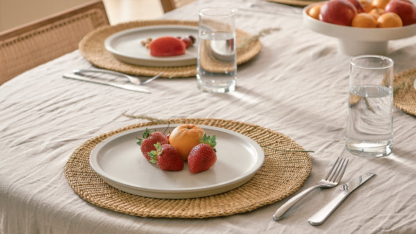 Dining table setting with plates, glasses, and fruit on a textured tablecloth.