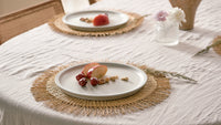 Table setting with plates, fruits, and a vase on a white tablecloth.