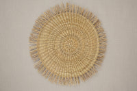 Round woven placemat with fringes on a beige background