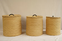 Three woven laundry baskets with lids on a light background