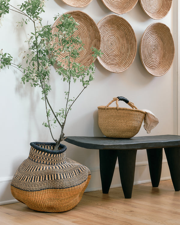 Woven basket and vase on a wooden floor with decorative woven plates on the wall.