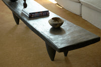 Long dark wooden coffee table with a decorative bowl on a beige carpeted floor.